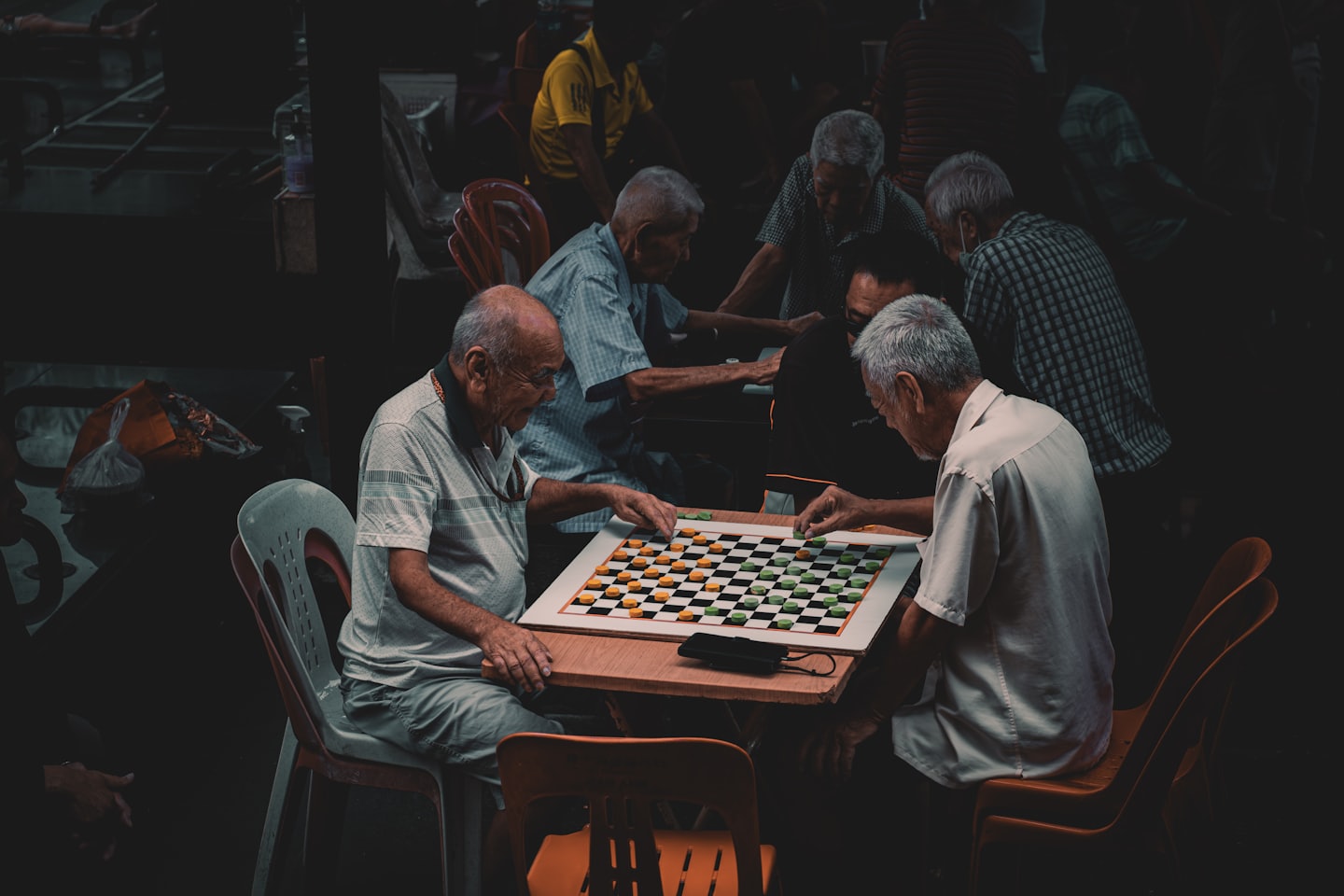 Skupina seniorov mužov hrá stolovú hru DÁMA v herni.