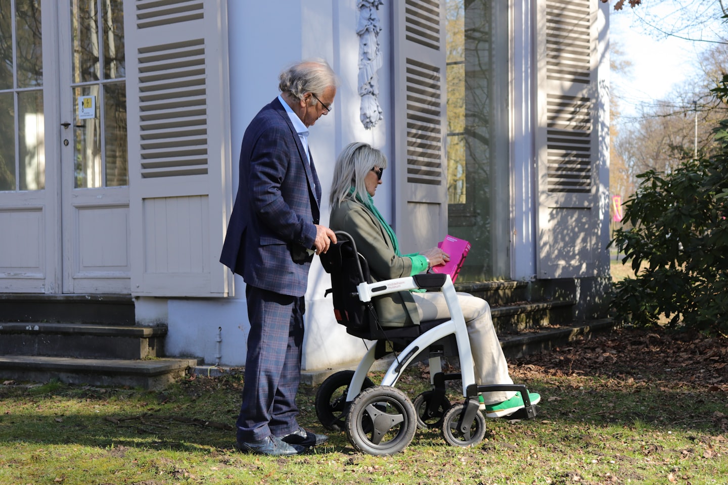 Seniori muž a žena. Muž tlačí ženu a invalidnom vozíku.