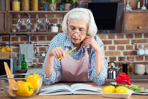 Staršia žena v kuchyni skúša nový recept podľa knihy – zvedavosť a chuť učiť sa nové veci.